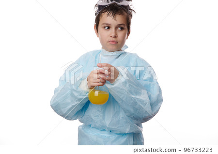 Multi-ethnic thoughtful smart teenage schoolboy in lab coat, holding a glass flask with yellow chemical liquid substance, doing experiments, isolated over white background. Chemistry Science concept Multi-ethnic thoughtful smart teenage schoolboy in lab coat, holding a glass flask with yellow chemical liquid substance, doing experiments, isolated over white background. Chemistry Science concept 96733223