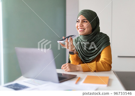 Young Muslim Woman In Hijab Recording Voice Message On Smartphone In Office Young Muslim Woman In Hijab Recording Voice Message On Smartphone In Office 96733546