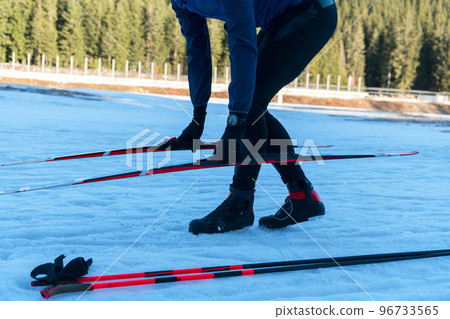 Handsome male athlete with cross country skis preparing equipment for training in a snowy forest. Checking smartwatch. Healthy winter lifestyle.  96733565