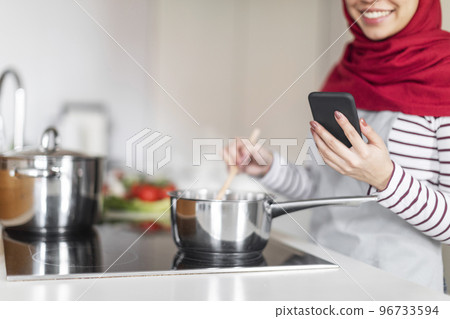 Cropped of woman in hijab cooking and using smartphone Cropped of woman in hijab cooking and using smartphone 96733594
