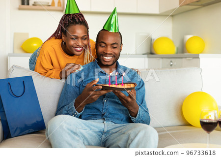 Happy african american wife surprising her husband with handmade birthday pie, man blowing candles and smiling 96733618