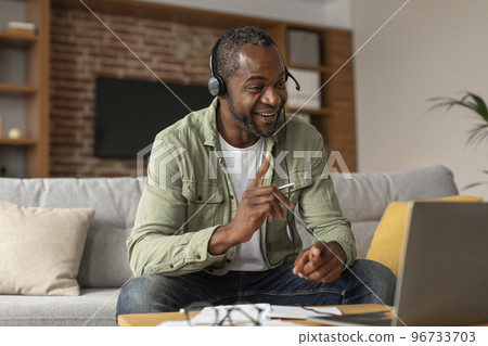 Happy busy middle aged african american male in headphones looking at laptop, gesturing 96733703