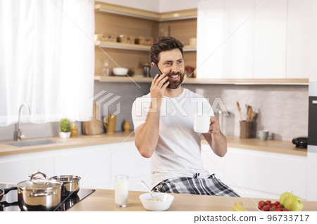 Happy adult caucasian guy with beard in white t-shirt drinks cup of coffee, calls by phone 96733717