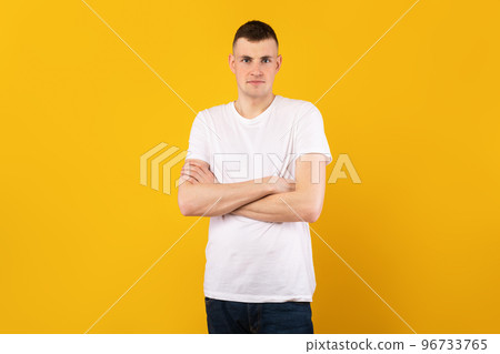 Male portrait. Handsome caucasian guy with folded arms looking at camera, wearing t-shirt, posing over yellow background Male portrait. Handsome caucasian guy with folded arms looking at camera, wearing t-shirt, posing over yellow background 96733765