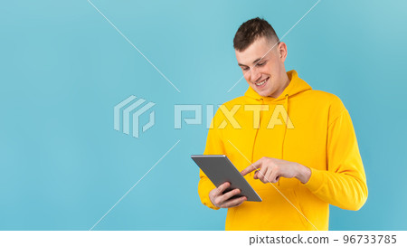 Modern technologies concept. Young man browsing web on digital tablet over blue studio background, panorama, free space Modern technologies concept. Young man browsing web on digital tablet over blue studio background, panorama, free space 96733785