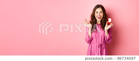 Excited young woman showing engagement ring, getting married, smiling happy, talking about wedding day, receive marriage proposal, standing over pink background Excited young woman showing engagement ring, getting married, smiling happy, talking about wedding day, receive marriage proposal, standing over pink background 96734097