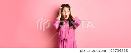 Young scared woman holding hands on head and gasping troubled, staring left at copyspace, standing over pink background Young scared woman holding hands on head and gasping troubled, staring left at copyspace, standing over pink background 96734218