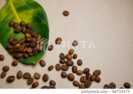 Large yellow-green leaf and coffee grains scattered on a white background Large yellow-green leaf and coffee grains scattered on a white background 96734373