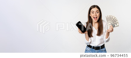 Enthusiastic young woman winning money, showing smartphone app interface and cash, microcredit, prize concept, standing over white background 96734455