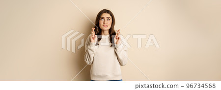 Hopeful worried girl cross fingers, making wish, standing over beige background 96734568