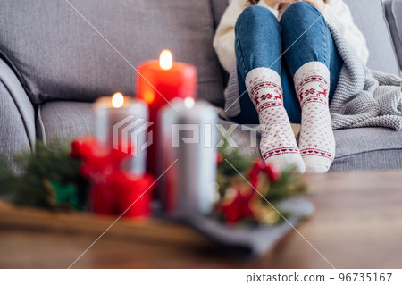 Female feet in xmas woolen socks and cozy Christmas mood candles composition for hygge home on the coffee table. Interior and home coziness concept. Winter and Christmas holidays. Selective focus. Female feet in xmas woolen socks and cozy Christmas mood candles composition for hygge home on the coffee table. Interior and home coziness concept. Winter and Christmas holidays. Selective focus. 96735167