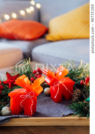 Christmas cozy mood composition for hygge home decor. Deer shape red candles, fresh green pine branches and festive Xmas decor on the tray on the coffee table in living room. Vertical. Selective focus Christmas cozy mood composition for hygge home decor. Deer shape red candles, fresh green pine branches and festive Xmas decor on the tray on the coffee table in living room. Vertical. Selective focus 96735169