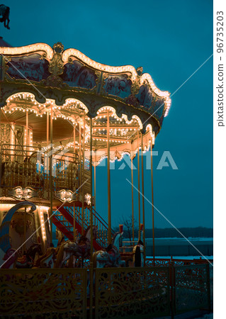 Children's Carousel roundabout, galloper at an amusement park in the evening at night illumination. Outdoor vintage colorful luminous. Blue background. New year, christmas entertainment mood concept. 96735203