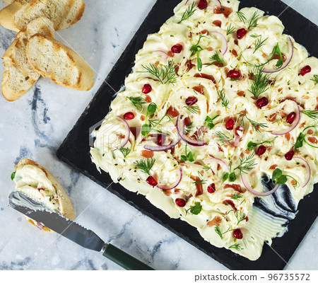Flat lay of a butter board topped with red onions, pomegranate seeds and garnished with dill leaves and micro green. Table top view Flat lay of a butter board topped with red onions, pomegranate seeds and garnished with dill leaves and micro green. Table top view 96735572