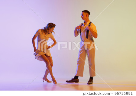 Beautiful girl and man in retro style costumes dancing incendiary dances isolated on gradient lilac color background in neon light. Concept of art, 60s, 70s culture Beautiful girl and man in retro style costumes dancing incendiary dances isolated on gradient lilac color background in neon light. Concept of art, 60s, 70s culture 96735991