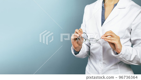 Hands of female doctor ophthalmologist or optician holds pair of glasses. Minimal blue background. Copy space. Optics oculist, eye test checkups. Medicine mockup template Hands of female doctor ophthalmologist or optician holds pair of glasses. Minimal blue background. Copy space. Optics oculist, eye test checkups. Medicine mockup template 96736364