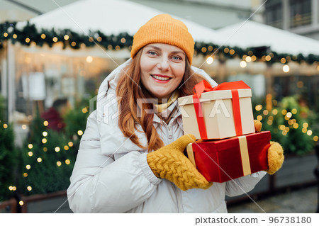 Happy young beautiful excited woman holding gift boxes in hands and smile on winter street. Winter holidays sale. Concept of shopping, holidays and happiness christmas. 96738180