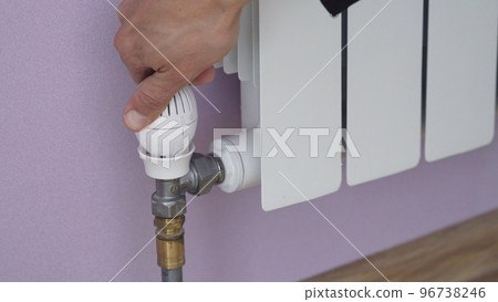 Closeup of hand of man setting to minimum temperature on radiator by using thermostat Closeup of hand of man setting to minimum temperature on radiator by using thermostat 96738246