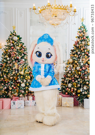 a bunny doll in a blue snow maiden costume in a room with Christmas trees. a bunny doll in a blue snow maiden costume in a room with Christmas trees. 96738433
