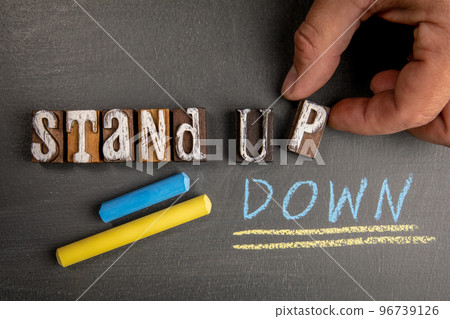 Stand Up and Stand Down. Wooden letter blocks on a dark chalkboard background Stand Up and Stand Down. Wooden letter blocks on a dark chalkboard background 96739126