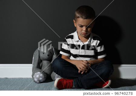Sad little boy with toy near black wall. Domestic violence concept 96740278