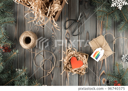 Handmade gift box in festive package decorated with rainbow postcard, top view. Spruce branches, filling material and tools. Christmas or New Year holiday concept, LGBT symbol, homosexual orientation 96740375