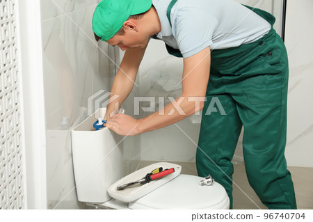 Professional plumber repairing toilet tank in bathroom 96740704