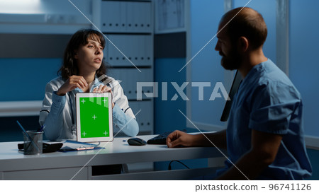Physician holding tablet computer pointing at green screen chroma key template while discussing patient disease report with assistant. Team working over hours at medical expertise in hospital office Physician holding tablet computer pointing at green screen chroma key template while discussing patient disease report with assistant. Team working over hours at medical expertise in hospital office 96741126