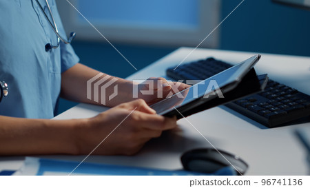 Close up of medical assistant holding tablet computer analyzing patient expertise, checking illness diagnosis report working after hours at health care treatment in hospital office. Medicine service Close up of medical assistant holding tablet computer analyzing patient expertise, checking illness diagnosis report working after hours at health care treatment in hospital office. Medicine service 96741136