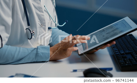 Close up of general practitioner holding tablet computer analyzing radiography while working over hours at medical expertise in hospital office. Doctor planning medication treatment for patient Close up of general practitioner holding tablet computer analyzing radiography while working over hours at medical expertise in hospital office. Doctor planning medication treatment for patient 96741144