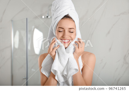 Young woman wiping face with towel in bathroom 96741265