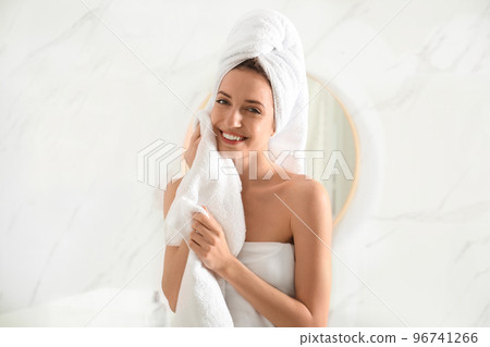 Young woman wiping face with towel in bathroom Young woman wiping face with towel in bathroom 96741266