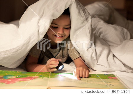 Little boy with flashlight reading book under blanket at home 96741564