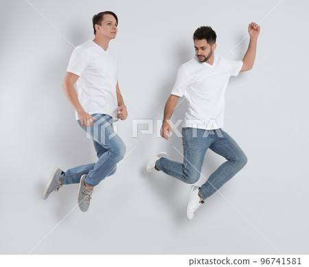 Young men in stylish jeans jumping on light background Young men in stylish jeans jumping on light background 96741581