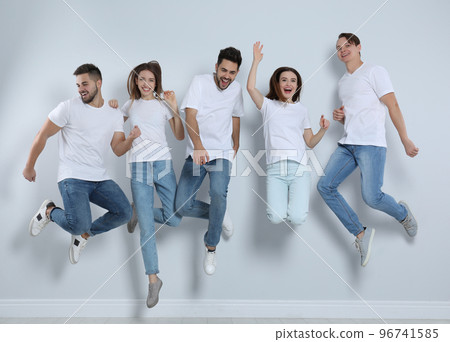 Group of young people in stylish jeans jumping near light wall 96741585