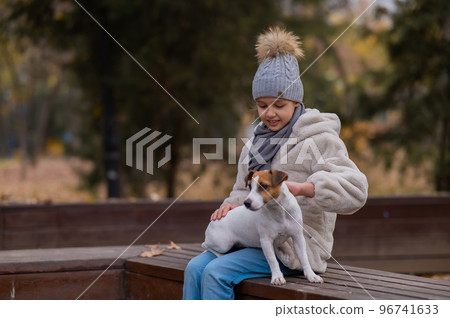 Caucasian girl sits on a bench with a dog Jack Russell Terrier for a walk in the autumn park. Caucasian girl sits on a bench with a dog Jack Russell Terrier for a walk in the autumn park. 96741633