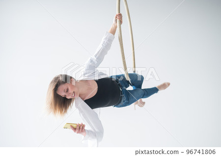 Caucasian female gymnast doing aerial hoop exercises and using smartphone. Caucasian female gymnast doing aerial hoop exercises and using smartphone. 96741806