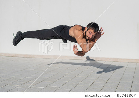 A man in black sportswear jumps while doing push-ups outdoors. A man in black sportswear jumps while doing push-ups outdoors. 96741807