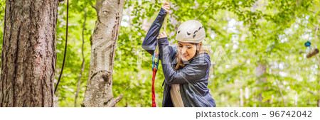 BANNER, LONG FORMAT Happy women girl female gliding climbing in extreme road trolley zipline in forest on carabiner safety link on tree to tree top rope adventure park. Family weekend children kids 96742042
