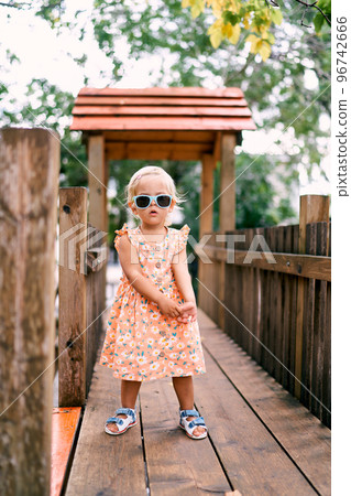 Little girl in sunglasses posing on a wooden bridge in the playground. High quality photo Little girl in sunglasses posing on a wooden bridge in the playground. High quality photo 96742666