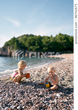 Little boy and girl playing with toy buckets on a pebble beach. High quality photo Little boy and girl playing with toy buckets on a pebble beach. High quality photo 96742675