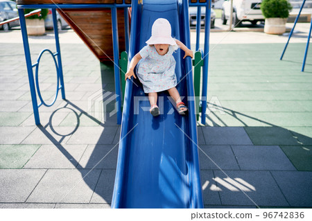 Little girl in a panama slides down a slide with her mouth open. High quality photo 96742836