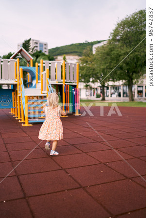 Little girl walks along the playground towards a colorful slide. High quality photo 96742837