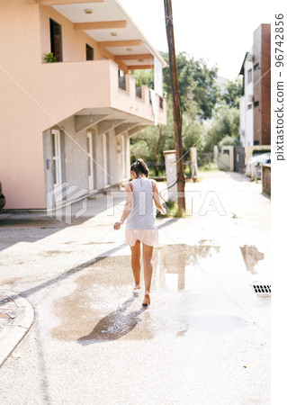 Young woman walks barefoot through puddles on the asphalt. Back view. High quality photo 96742856