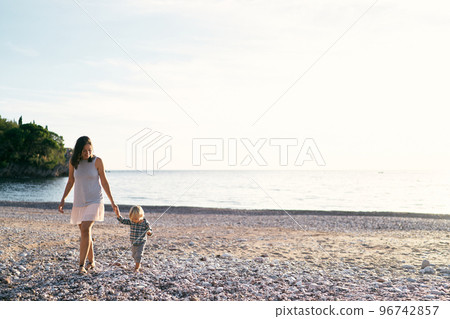 Mom and little girl are walking along the seashore holding hands. High quality photo 96742857