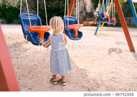 Little girl stands near the swing. Back view. High quality photo Little girl stands near the swing. Back view. High quality photo 96742888