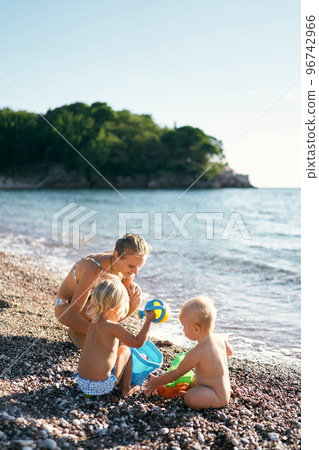 Mom plays with a little girl and a boy with toys on the seashore. High quality photo 96742966