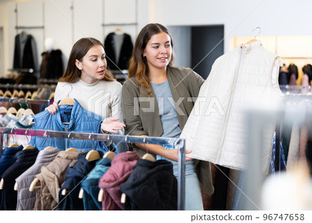 Joyful young women choosing between white and blue waistcoats in a clothing store Joyful young women choosing between white and blue waistcoats in a clothing store 96747658