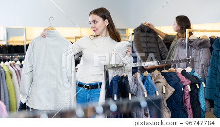 Young female choosing between leather jacket and white gilet before autumn season in a store Young female choosing between leather jacket and white gilet before autumn season in a store 96747784