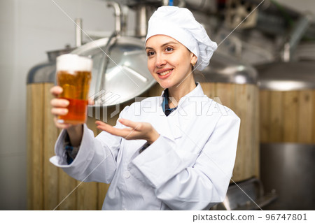 Successful female brewmaster holding glass of foamy ale 96747801